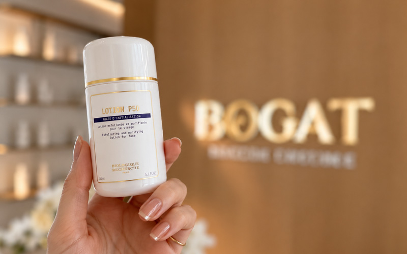 A bottle of Biologique Recherche Lotion P50 held in front of the BOGAT brand wall at Bogat Aesthetics & Wellness in Hallandale Beach, Florida.
