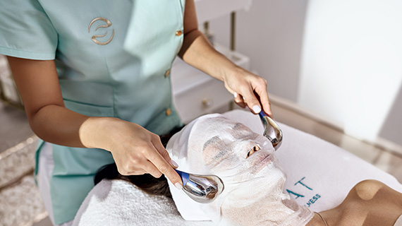 A Bogat aesthetician glides stainless-steel cooling globes over a client's treatment mask during a facial in Hallandale Beach.
